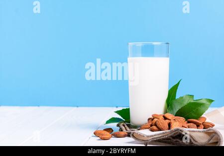 Laktosefreies Milchkonzept, Glas mit Mandelmilchnüssen auf weißem Tisch auf blauem Hintergrund Stockfoto