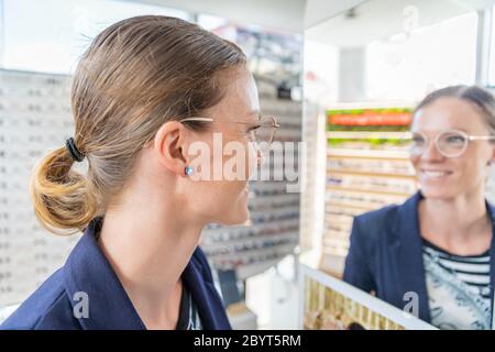 Geschäftsfrau probiert in einem Optikgeschäft eine Brille vor einem Spiegel aus Stockfoto