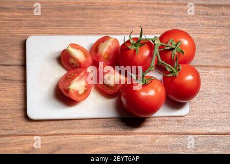 Reife rote Tomaten auf weißem Schneidebrett mit vielen Stück gehackte Tomaten auf braunem Holztisch Stockfoto