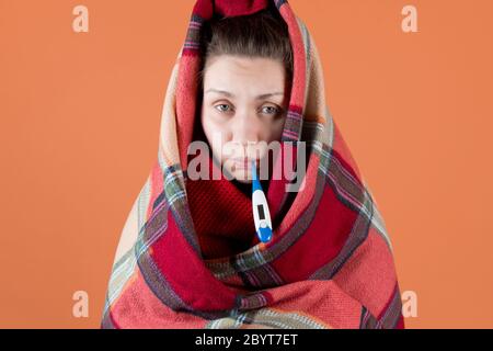 Das kranke Mädchen wickelte sich in ein Karli und hält Ein Thermometer in ihrem Mund Stockfoto