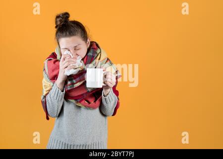 Mädchen in einer Decke gewickelt wischt ihre Nase mit einem Serviette und hält ein heißes Getränk Stockfoto