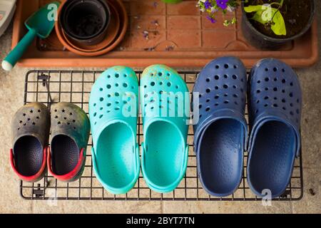 Drei Paar bunte Gummi-Gartensandalen oder Clogs, für jedes Familienmitglied, auf einem Regal im Garten. Draufsicht. Stockfoto