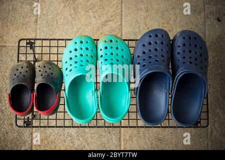 Drei Paar bunte Gummi-Gartensandalen oder Clogs, für jedes Familienmitglied, auf einem Regal im Garten. Draufsicht. Stockfoto