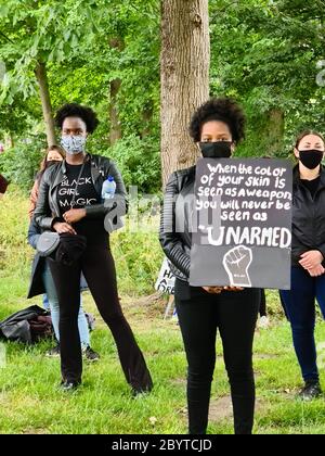 Amsterdam, Niederlande. Juni 2020. Junge schwarze Frauen in schwarzer Kleidung, die das Schild halten: Wenn die Farbe Ihrer Haut als Waffe gesehen wird, werden Sie nie als "unbewaffnet" gesehen werden. Schätzungsweise 11.500 Teilnehmer versammelten sich friedlich im Nelson Mandela Park zur zweiten Black Lives Matter-Manifestation in Amsterdam. Dieses Treffen wurde von den Bewohnern des Bijlmer, dem Bezirk mit der größten Bevölkerung von Afro-Niederländisch in Amsterdam organisiert. Seit Jahrzehnten sind Mitglieder der schwarzen Gemeinschaft in der Bijlmer Opfer von Diskriminierung, Rassismus..Quelle: Steppeland/Alamy Live News Stockfoto