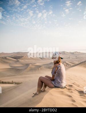 Frau sitzt auf einer Düne, lächelt und Wolken Stockfoto