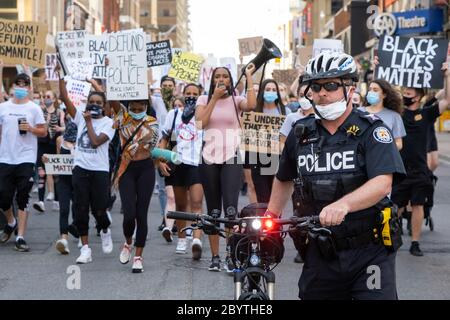 Ein Polizist geht vor einer Menge von Black Lives Matter Demonstranten, während sie die Strafverfolgung in Toronto, Ontario verurteilen. Stockfoto