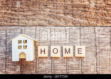 Miniatur-Spielzeughaus mit Inschrift HOME Buchstaben Wort auf Holzhintergrund. Hypothek Immobilien Versicherung Traum Haus Konzept. Flach, oben liegend, Kopieplatz Stockfoto