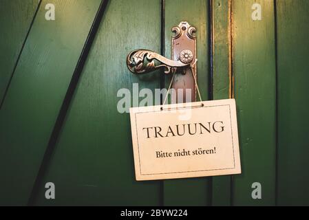 Geschlossene grüne Holztüren mit dekorativen Beschlägen. Am Griff hängendes weißes Schild 'Hochzeit, bitte nicht stören!' Konzept für Hochzeitstag. Stockfoto