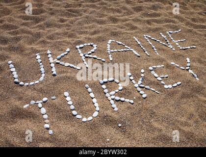 Worte der Ukraine, der Türkei und Lächeln aus Kieselsteinen auf Sand Strand im Sommer Stockfoto