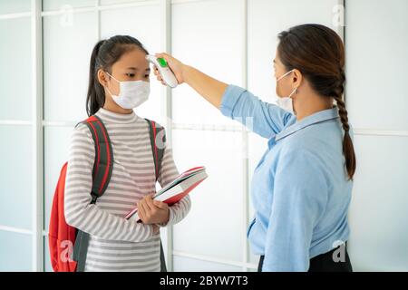 Asiatische Frau Lehrer mit Thermometer Temperatur Screening Schüler für Fieber gegen die Ausbreitung von COVID-19, während Schüler wieder in die Schule, Neu Stockfoto
