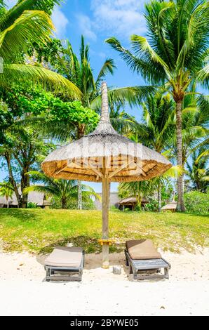 Liegestühle am Strand mit Strohschirm unter den Palmen. Romantischer Sommerurlaub und Entspannung. Ruhige und ruhige Szene im tropischen Paradies. Stockfoto