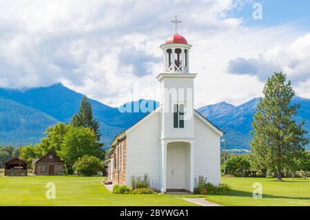 Eine schöne alte Kapelle und rustikale Hütten in Montana mit den Rocky Mountains in der Ferne an einem sonnigen Tag Stockfoto