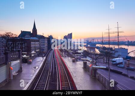Landungsbrücken Bahnhof in Hamburg, Deutschland bei Sonnenaufgang, früh am Morgen, mit Tracer von Rücklicht des vorbeifahrenden Zuges. Elbufer, Innenstadt Stockfoto
