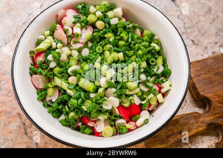 Salat mit Rettich und Zwiebel in weißem Metallplatte auf dem Tisch in der Nähe von Holzbrett, qualitativ hochwertiges Foto Stockfoto