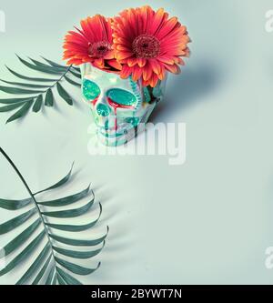 Totenkopf mit korallenfarbenen Gerbera Gänseblümchen und Palmenblättern auf Kachelgrünem Hintergrund. Kreatives Konzept. Surreales Feeling, gespenstische Atmosphäre. Dia de Stockfoto