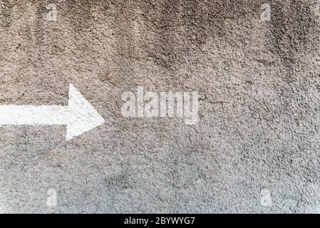 Pfeil mit einer weißen Linie auf einer Steinwand mit negativem Raum und Kopierraum gemalt, um die Richtung anzuzeigen. Stockfoto