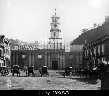 Bild der Plaza Sotomayor im Jahr 1867. Im Zentrum befindet sich die alte Intendencia de Valparaíso, ein Gebäude, das ursprünglich als Zollhaus gebaut wurde. An der Fassade sind schwarze Punkte zu sehen, darunter einer an der Nummer vier auf der Uhr, das sind die Markierungen, die die Kanonenkugeln während des Bombardements von Valparaíso hinterlassen haben, das ein Jahr zuvor von der spanischen Flotte ausgeführt wurde Stockfoto