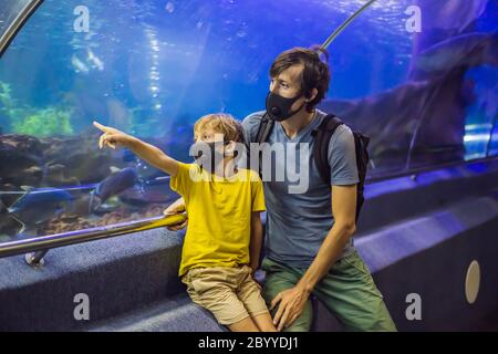 Vater und Sohn in medizinischen Masken schauen sich die Fische im Aquarium im Ozeanarium an. Nach dem Ende des Coronovirus gehen die Menschen in medizinischen Masken Stockfoto