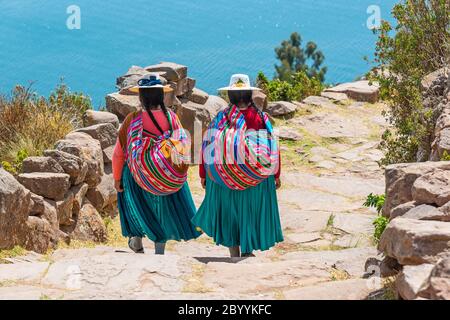 Zwei einheimische peruanische Quechua-Frauen in traditioneller Kleidung gehen die Treppe hinunter zum Hafen der Taquile-Insel, Titicaca-See, Peru. Stockfoto