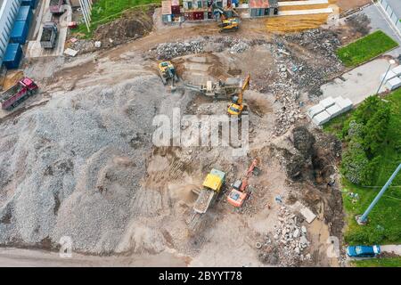 Arbeitsbagger auf dem Gelände eines abgerissenen Gebäudes. Verladung von Zementrückständen in die Zerkleinerungsanlage und den LKW-Boden, Draufsicht Stockfoto