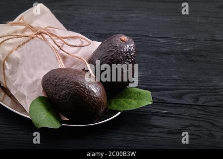 Dunkle Avocado haas, auf dunklem Holzhintergrund, Öko-Verpackung, Lebensmittelzustellung, Kopierraum. Stockfoto