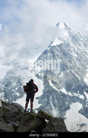 Vertikale Momentaufnahme des Touristen mit Rucksack, der mit dem Rücken zur Kamera steht und die Schönheit des Ober Gabelhorn in den Schweizer Alpen genießt Stockfoto