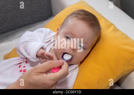 Nettes kleines Mädchen auf dem Bett liegend und essen Reissuppe mit Löffel. Mutter füttert ihr Baby Mädchen. Das Mädchen ist vier Monate alt. Stockfoto