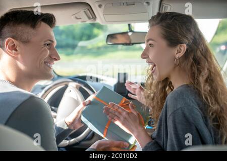 Lächelnder Mann, der der freudigen Frau im Auto die Schachtel gibt Stockfoto
