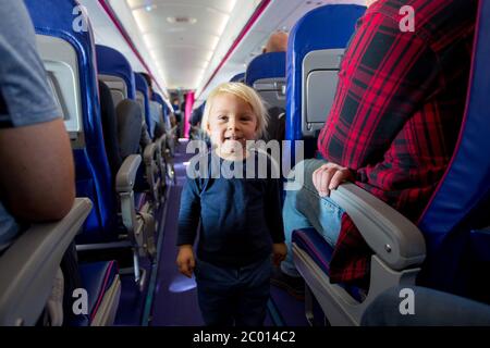 Niedlicher Kleinkind Junge im Flugzeug, spielen auf dem Weg zwischen den Sitzen, lächelnd glücklich. Familienreise mit Kindern Konzept Stockfoto