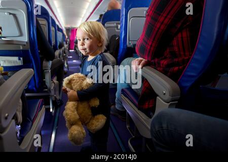 Niedlicher Kleinkind Junge im Flugzeug, spielen auf dem Weg zwischen den Sitzen, lächelnd glücklich. Familienreise mit Kindern Konzept Stockfoto