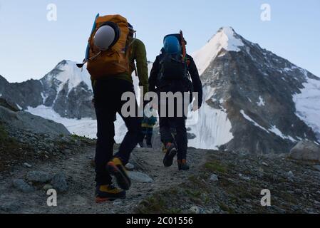 Zinal, Schweiz - 19. Juli 2019: Rückansicht von Reisenden mit Rucksäcken und Helmen, die nacheinander auf Hangstraßen laufen. Touristen klettern felsigen Bergweg. Konzept des Bergsteigens. Stockfoto