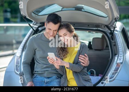 Frau mit Smartphone und Mann hockte auf Autokoffer. Stockfoto