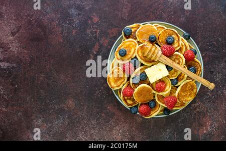 Trendige Küche - Haufen Mini-Pfannkuchen Müsli auf einem Teller mit Butter, Beeren und Honig. Stockfoto