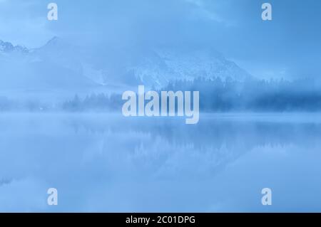 Berge spiegeln sich im See im dichten Nebel Stockfoto