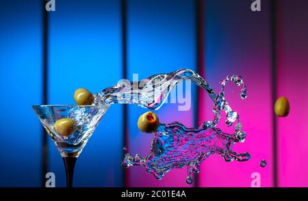 Martini und grüne Oliven im Glas. Spritzer auf einem bunten Hintergrund. Kopierbereich. Stockfoto