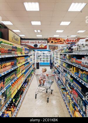 Budva, Montenegro - 10. juni 2020: Ein kleines Kind sitzt in einem Trolley vom Supermarkt. In der Abteilung mit Säften und Haushaltswaren. Stockfoto