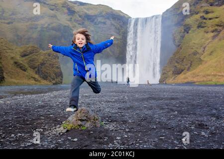 Niedliches Kind, das an einem bewölkten Tag bei Sonnenuntergang vor dem Skogafoss Wasserfall in Island läuft Stockfoto