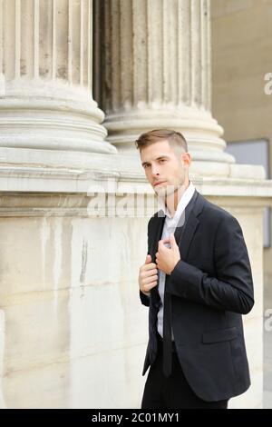 Junger Mann in schwarzem Anzug und Krawatte, der in Paris unterwegs ist, Säulen im Hintergrund. Stockfoto
