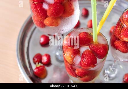 Erdbeere kaltes Getränk mit Eis im Glas auf weißem Hintergrund mit tropischen Blättern. Selektiver Fokus. Stockfoto