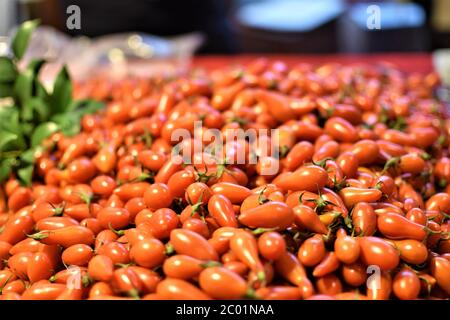 Süße, leckere, leuchtend rote, pflaumenförmige, reife Kirschtomaten, die auf einem Nachtmarkt verkauft werden Stockfoto