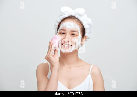 Glücklich junge asiatische Frau Anwendung schäumende Reinigungsmittel auf ihr Gesicht und tragen Handtuch auf ihren Kopf. Stockfoto
