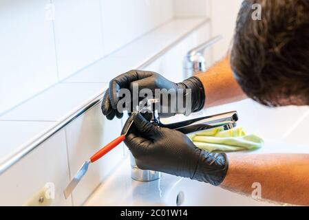 Ein Mann, der ein Waschbecken im Badezimmer mit einem Schaber und einem Mikrofasertuch reinigt, um Kalk und Flecken zu entfernen Stockfoto