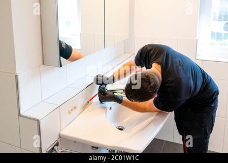 Ein Mann, der ein Waschbecken im Badezimmer mit einem Schaber und einem Mikrofasertuch reinigt, um Kalk und Flecken zu entfernen Stockfoto