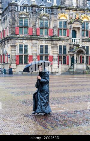 Lady in Black, die sich an einem nassen Morgen unter einem Regenschirm vor Regen schützt, in Markt, Delft, Südholland, Niederlande Stockfoto