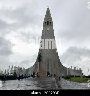 REYKJAVIK, ISLAND - 30. Juni 2018: Hallgrimskirkja, eine lutherische Pfarrkirche mit Leif Erikson Statur und Menschen am bewölkten Himmel. Cathedral Building w Stockfoto