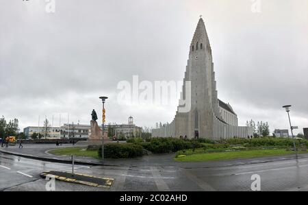 REYKJAVIK, ISLAND - 2. Juli 2018: Hallgrimskirkja, eine lutherische Pfarrkirche mit Leif Erikson Statur und Menschen am bewölkten Himmel. Kathedrale Gebäude wi Stockfoto