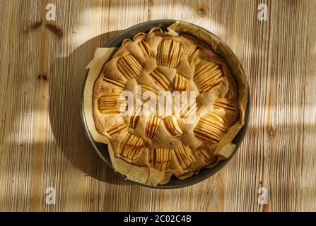 Runde Apfelkuchen frisch aus dem Ofen auf einem Holzbrett mit Textur und warmen Tönen. Stockfoto