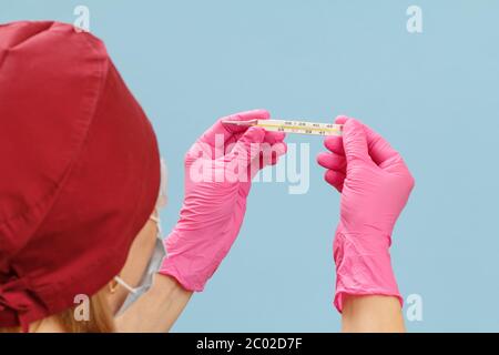 Nahaufnahme einer Ärztin in rosa Nitrilhandschuhen mit einem Quecksilberthermometer aus Glas. Selektiver Fokus auf ein Thermometer. Stockfoto