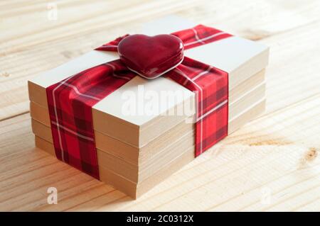 Vier Bücher mit einem gemusterten Band mit roten und weißen Quadraten und einem herzförmigen Ornament auf einem Holztisch gebunden. Stockfoto