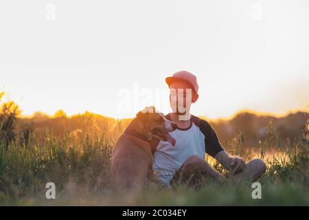 Der Mensch interagiert mit seinem Hund bei Sonnenuntergang, im Sommer. Haustiere und menschliche Freundschaft, kümmern, verbringen Zeit zusammen. Stockfoto